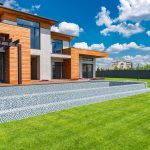 Exterior of contemporary residential house with panoramic windows glass doors and green lawn in yard on sunny day against blue sky with white clouds